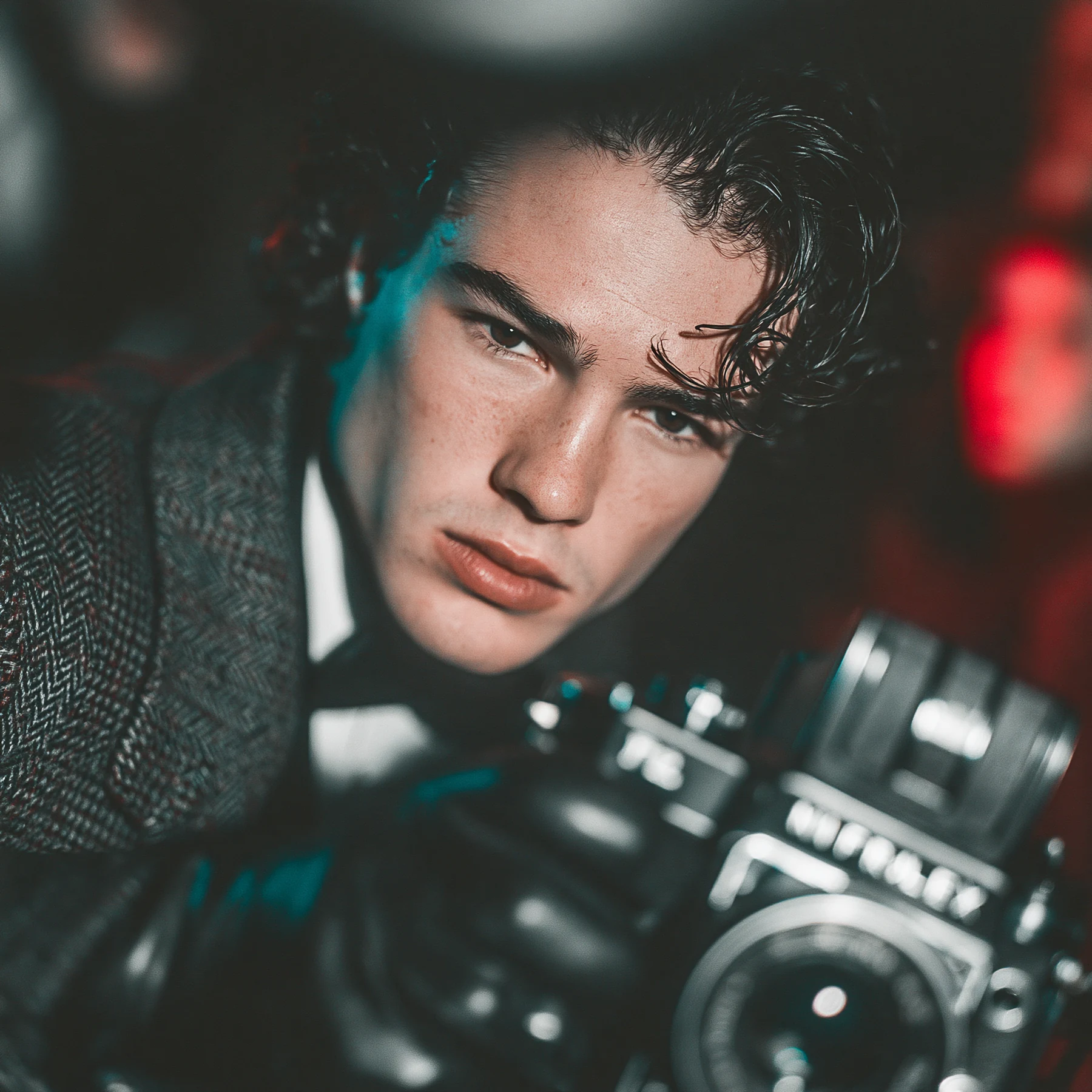 A close portrait with a camera, teal shadows and red light.