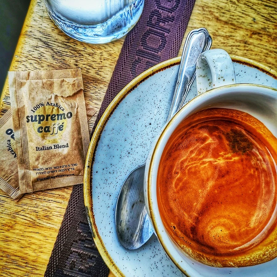 A coffee cup and saucer, a spoon and a paper packet on a sunlit table.