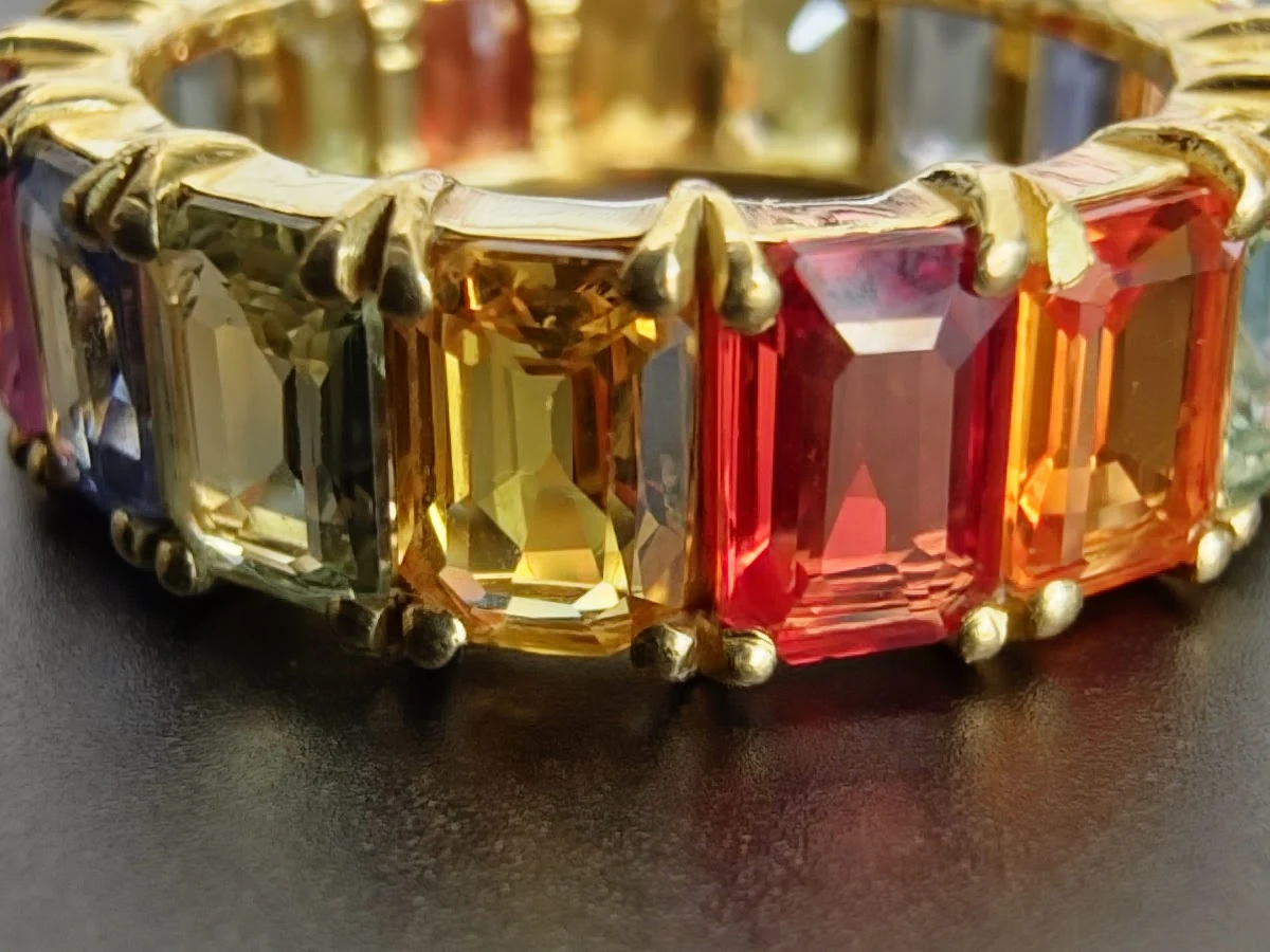 Close-up of a ring with a spectrum of rectangular coloured stones in a gold-coloured setting.